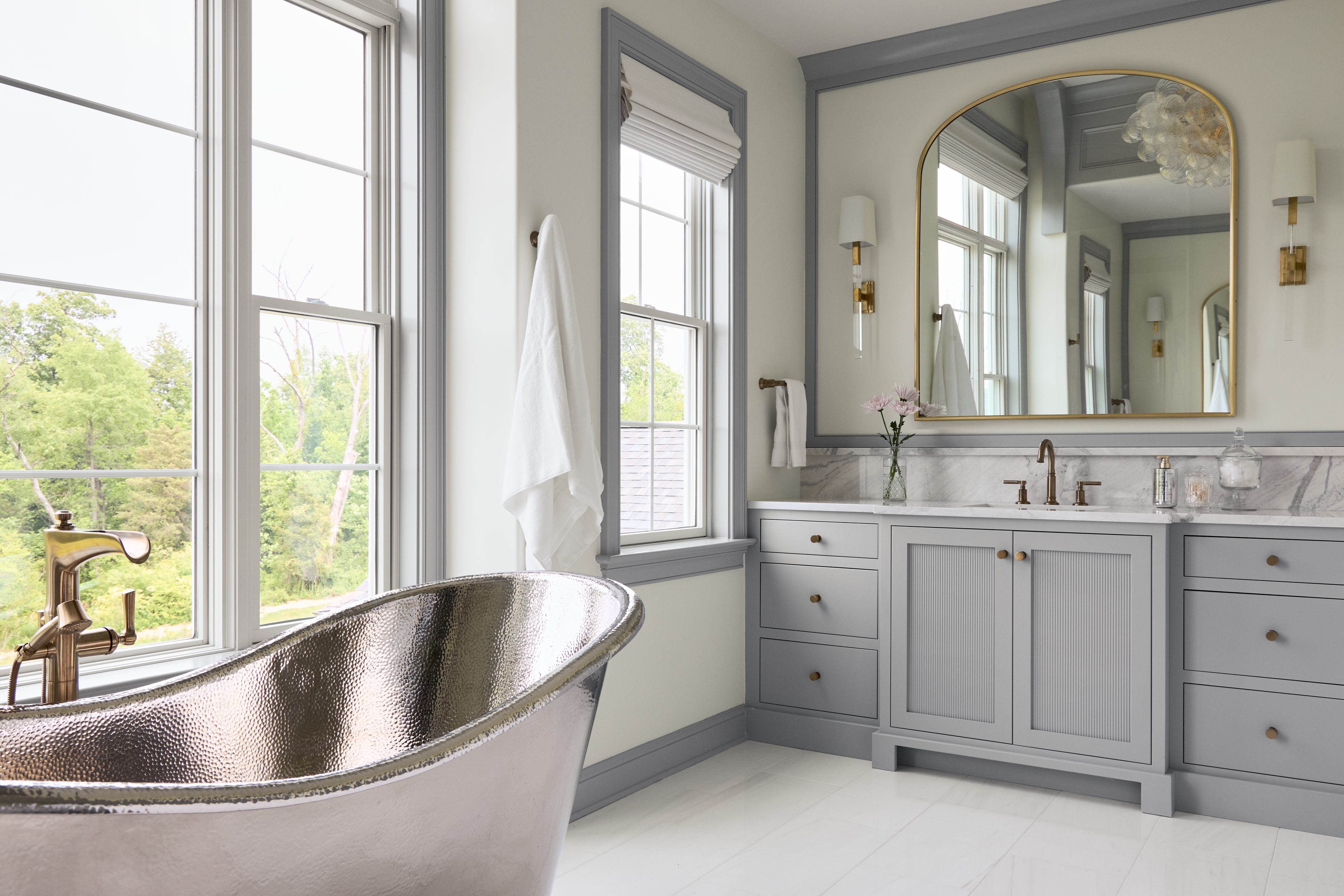 A Brushed Nickel Aurora 72 freestanding copper bathtub plated in nickel is set against a wall of bathroom windows and farrow and ball painted cabinetry