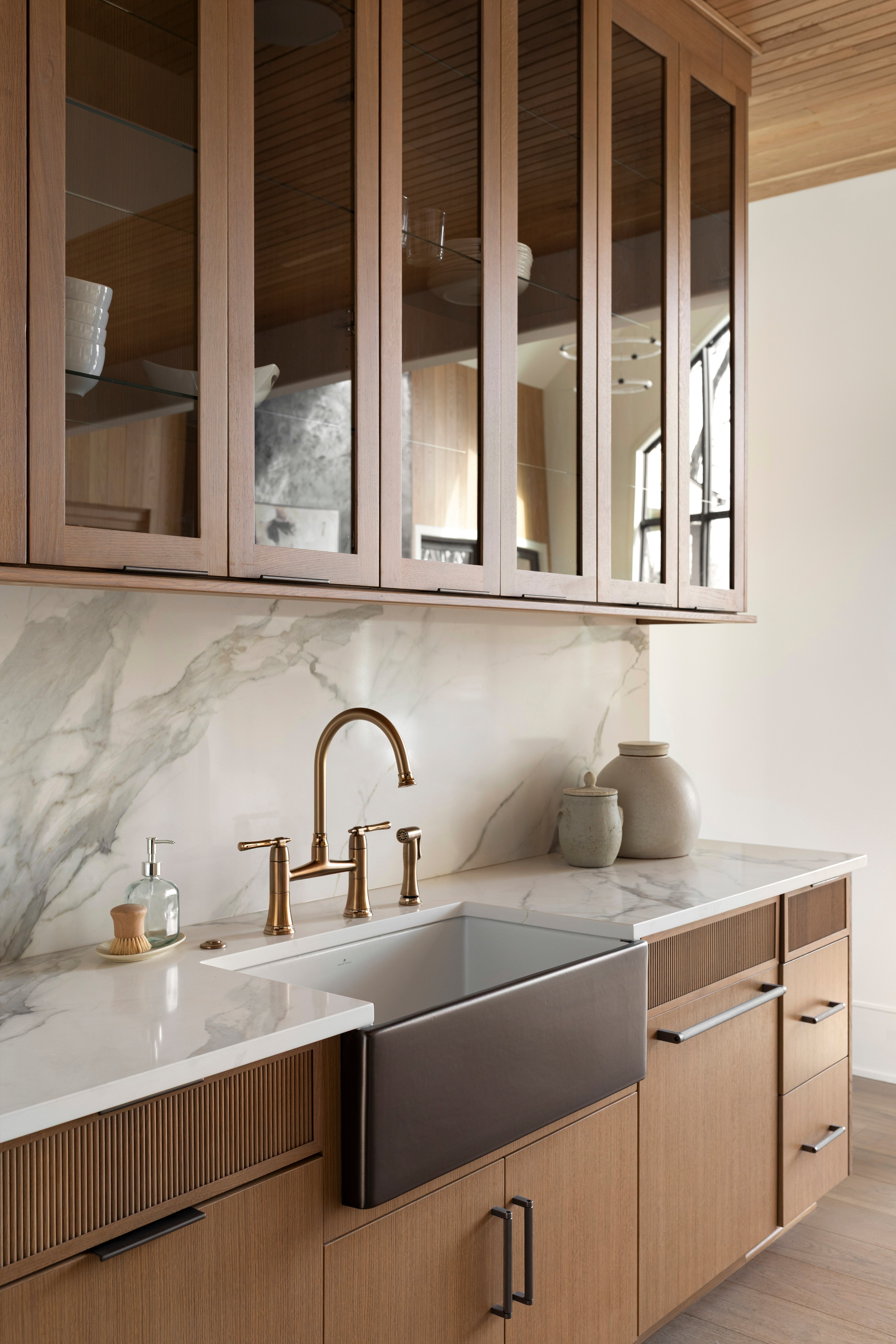 White oak kitchen cabinets with a marble countertop and marble slab backsplash, brass bridge faucet and fireclay kitchen sink with hand brushed precious metals glaze