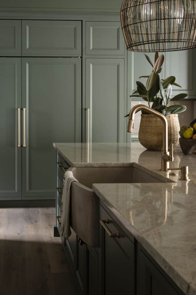 A creamy natural stone countertop is enhanced by a concrete kitchen sink and sage green cabinets