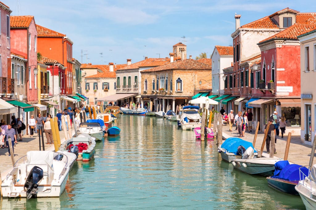 View of the Venetian houses with boats along the canal at the Islands of Murano in Venice. Famous tourist place.