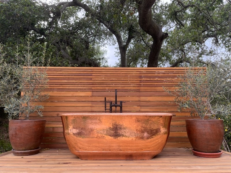 Surrounded by olive trees and centuries old oak trees, a freestanding copper bathtub creates a backyard oasis in Ojai, CA at actor Jason Baldoni's family home.