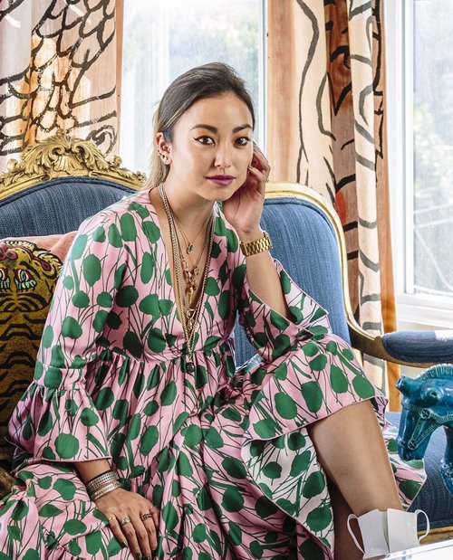 Interior Designer Noz Nozawa poses in her home for a portrait wearing a colorful pink dress with a green botanical overlay.