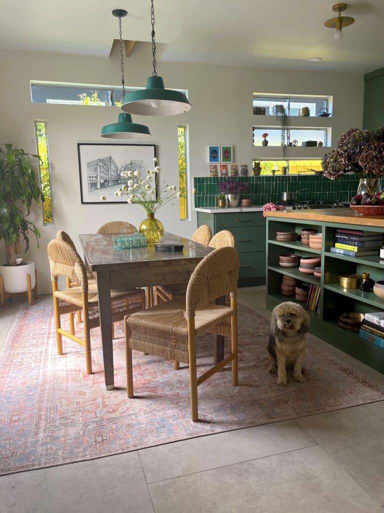 A jewel toned kitchen ripe with design inspiration features a cute puppy and an antique rug with Spanish modern chairs
