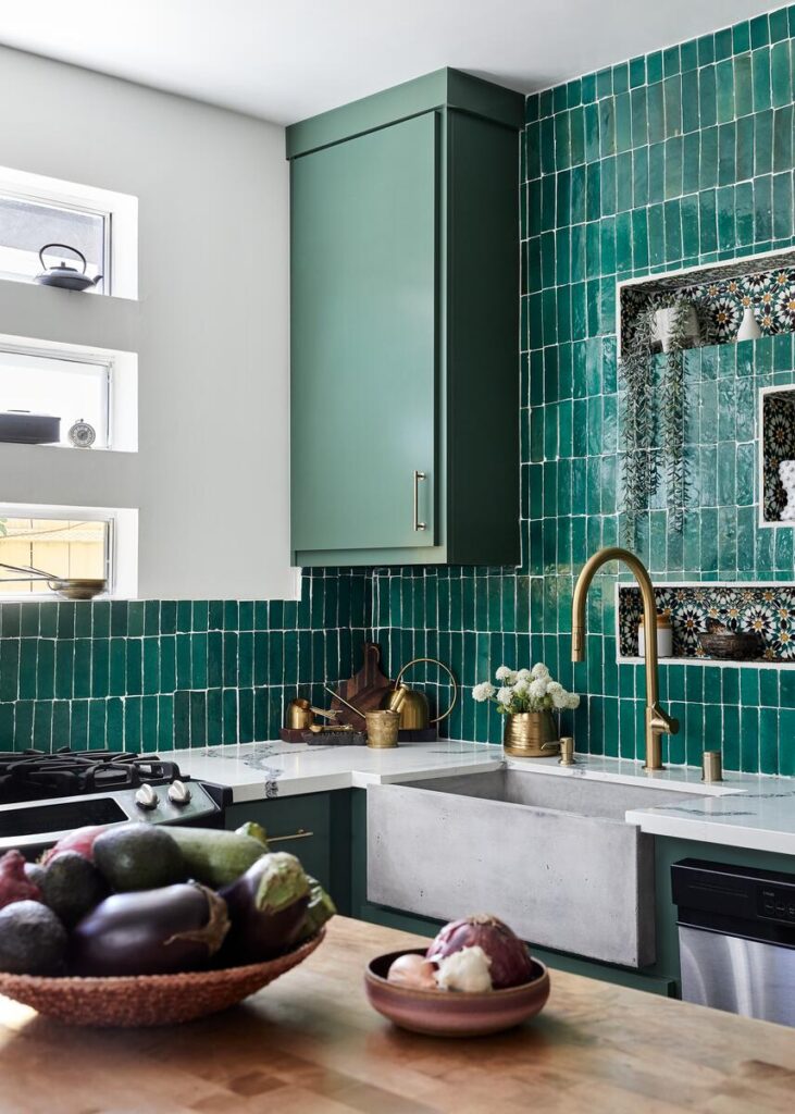 Kitchen displaying cabinets painted in Farrow & Ball’s Minster Green, the backsplash is clad in emerald green Zia Tile, and the concrete sink is by Native Trails