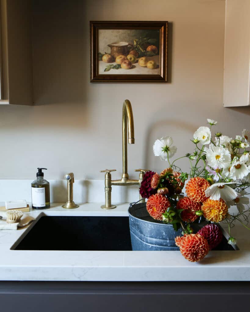 A black, NativeStone concrete sink set against brass fixtures. In the sink there's a silver bucket filled with colorful wildflowers. 