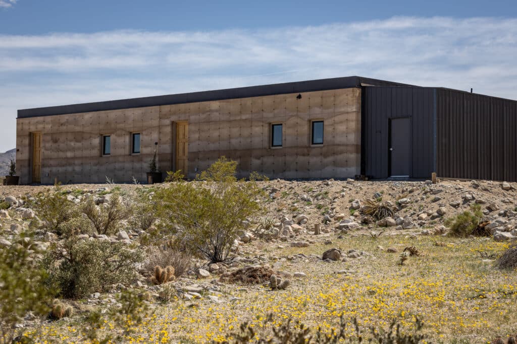 Rammed earth home placed in the middle of a dessert landscape with beautiful yellow flowers.