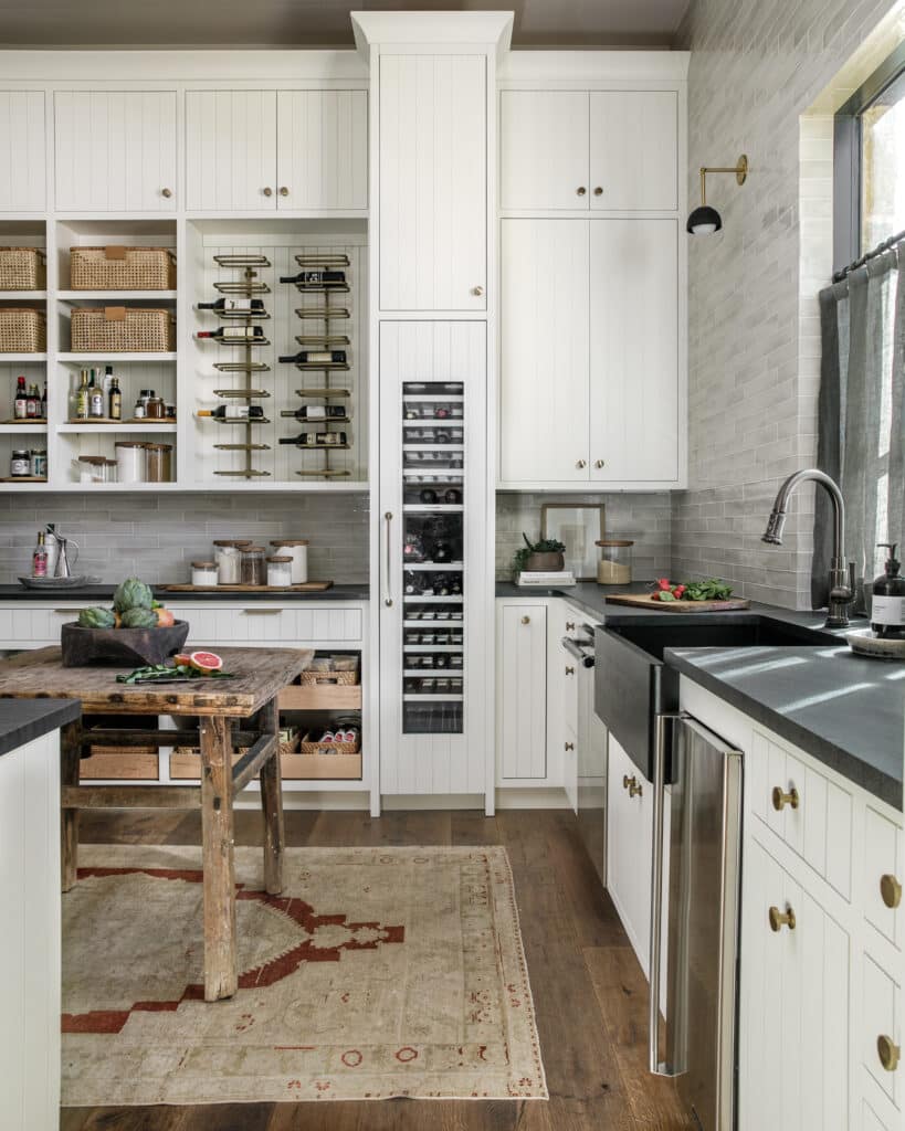 Large butlers pantry (aka dirty kitchen or scullery kitchen), featuring white wooden cabinets, soapstone countertops and weathered wood flooring make this space a 2025 kitchen and bath design trends  